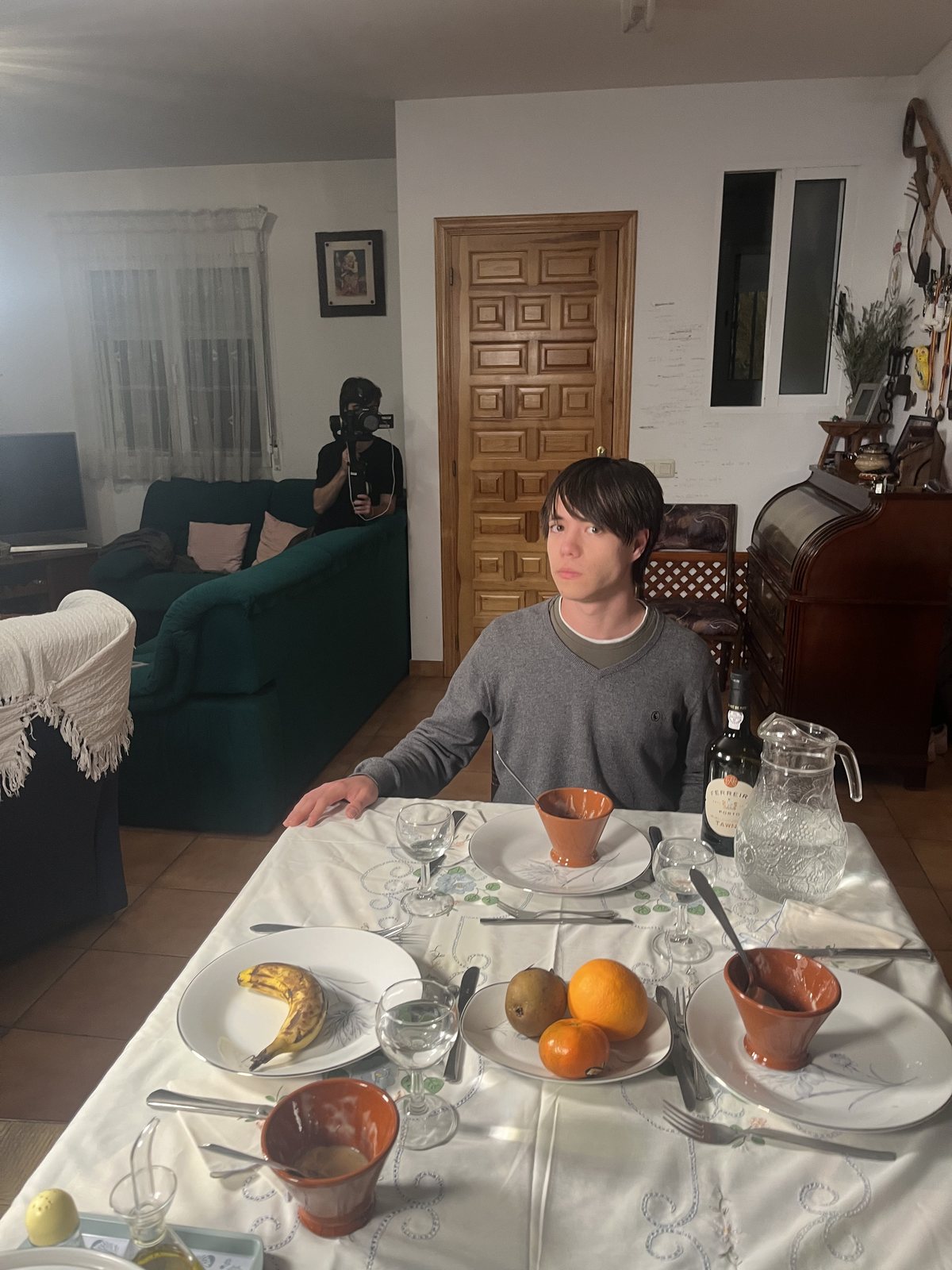 A scene set around a dining table with a camera operator in the background